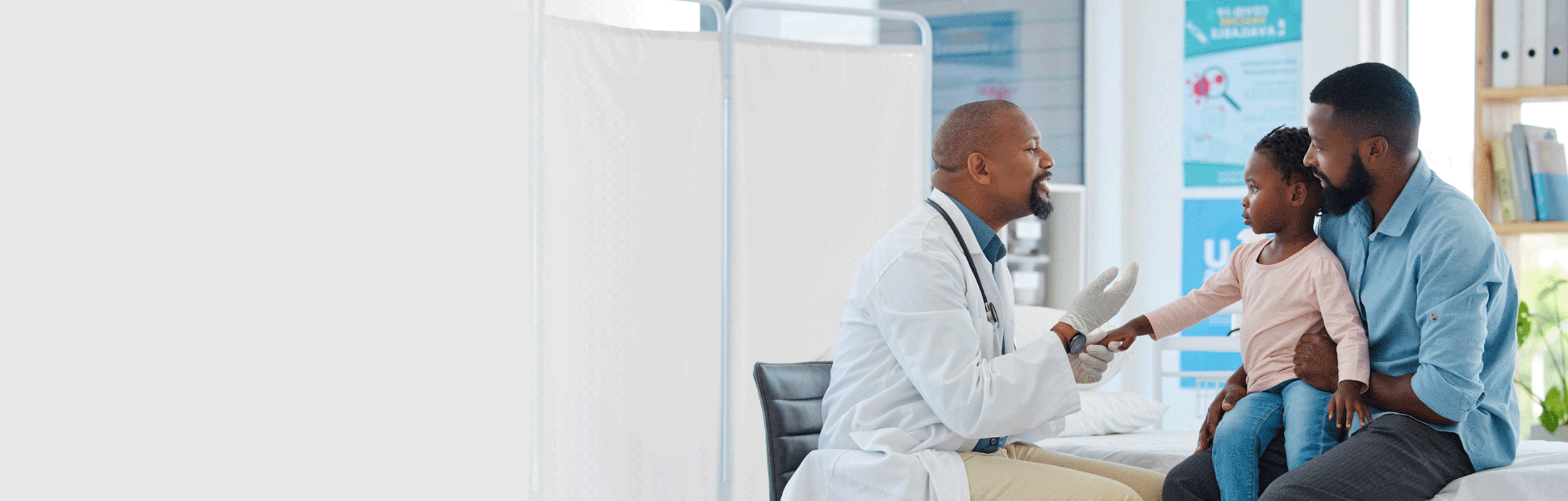 Doctor examines child's hand during check-up while seated on adult's lap in a medical clinic