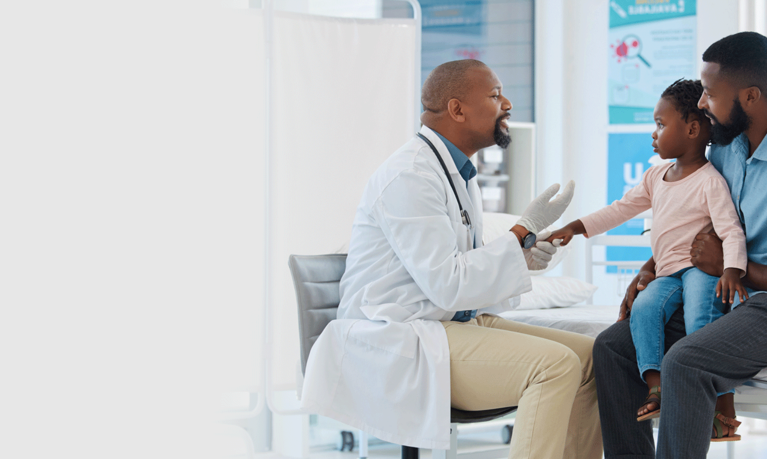 Doctor examines child's hand during check-up while seated on adult's lap in a medical clinic