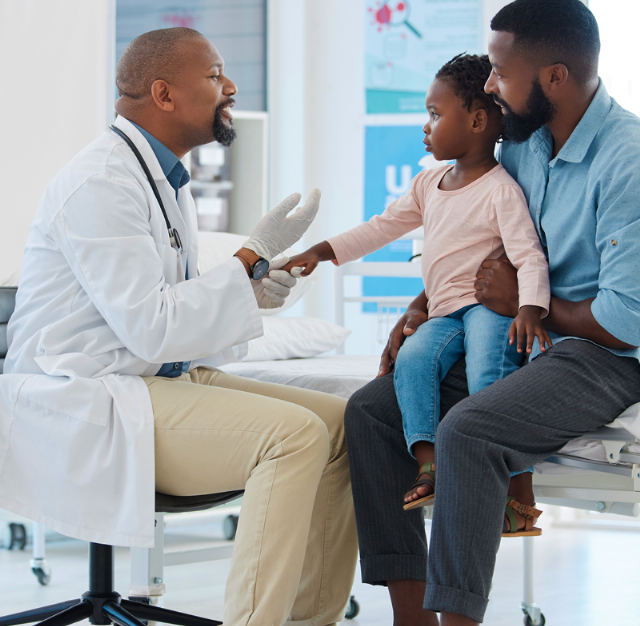 Doctor examines child's hand during check-up while seated on adult's lap in a medical clinic
